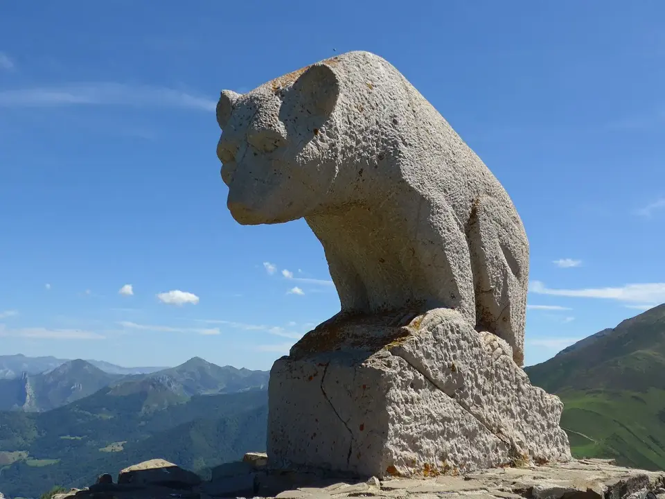 Escultura de piedra de un oso pardo en el collado de Llesba, con valles y montañas detrás