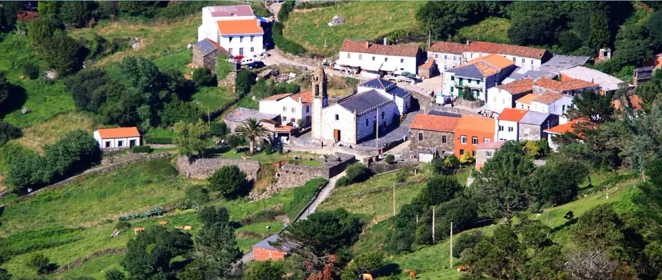 Vista panorámica del santuario y el caserío de San Andrés de Teixido entre prados verdes sobre el mar