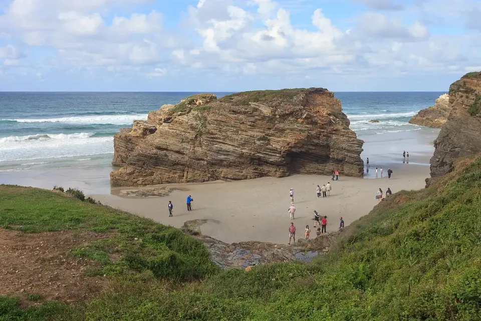 Gran roca de esquisto aislada sobre la arena en la playa de As Catedrais con marea baja y gente paseando
