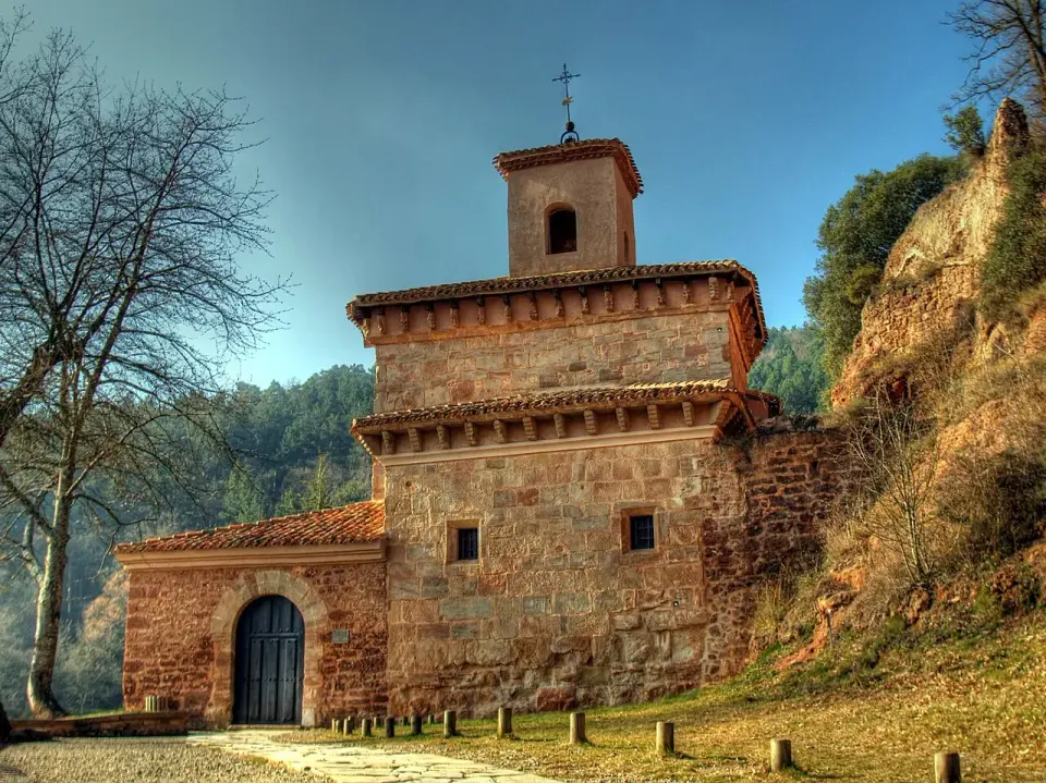 Monasterio de San Millán de Suso, de piedra rojiza, junto a la roca de la ladera y rodeado de bosque