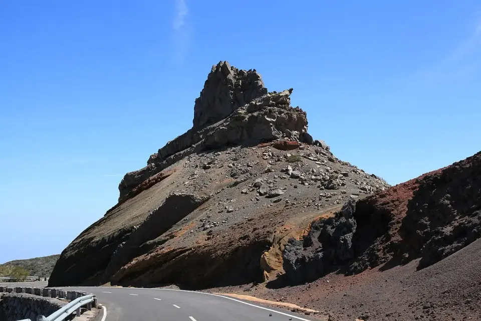 Carretera LP-4 bordeando un roque volcánico de piedra oscura en la zona alta de La Palma, bajo un cielo azul