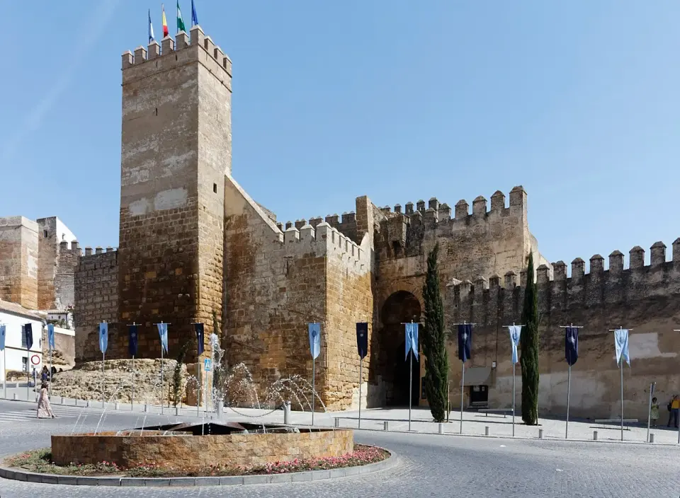 La Puerta de Sevilla de Carmona, una fortaleza de muros almenados y torre maciza junto a una rotonda con fuente