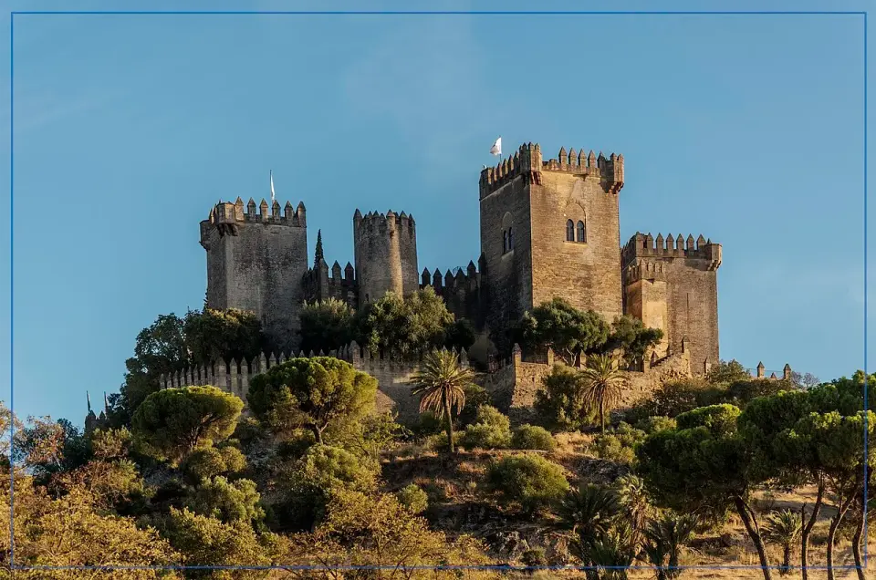 El castillo de Almodóvar del Río, con varias torres almenadas, sobre un cerro cubierto de pinos y vegetación