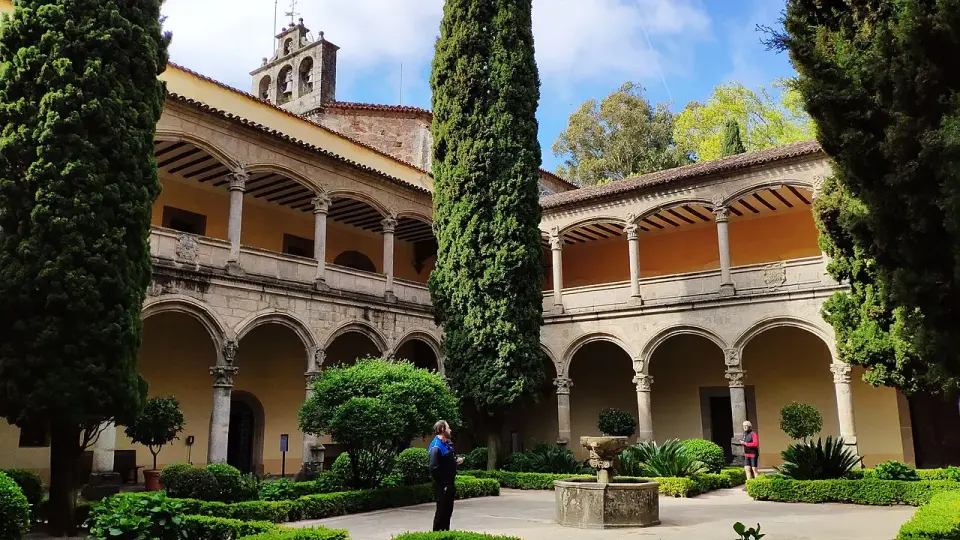 Claustro renacentista del monasterio de Yuste con dos pisos de arcos, cipreses y una fuente en el centro del patio
