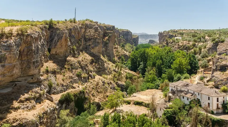 Cañón del río Alhama, con paredes de roca ocre, vegetación en el fondo y casas al borde del tajo en Alhama de Granada