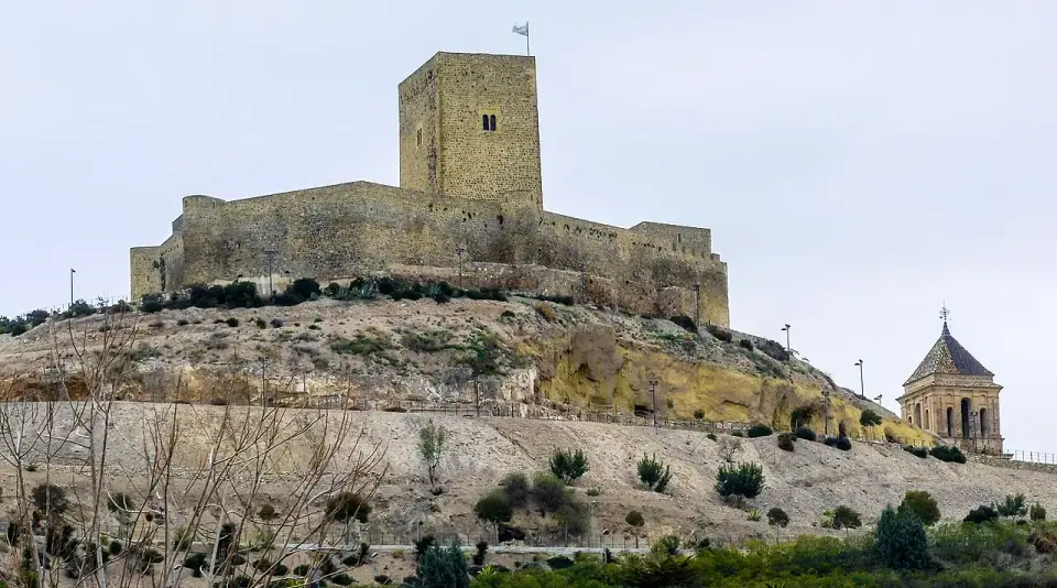 El castillo de Alcaudete, con su gran torre del homenaje, en lo alto de un cerro sobre el pueblo y la torre de una iglesia