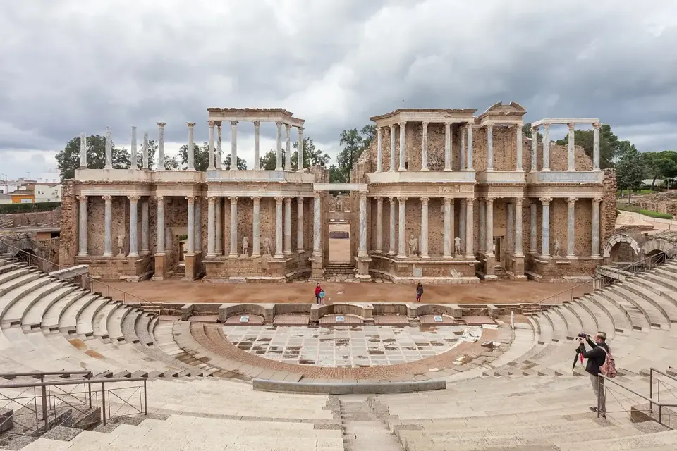 Escena columnada de dos pisos y graderío semicircular del teatro romano de Mérida, con visitantes en la orquesta