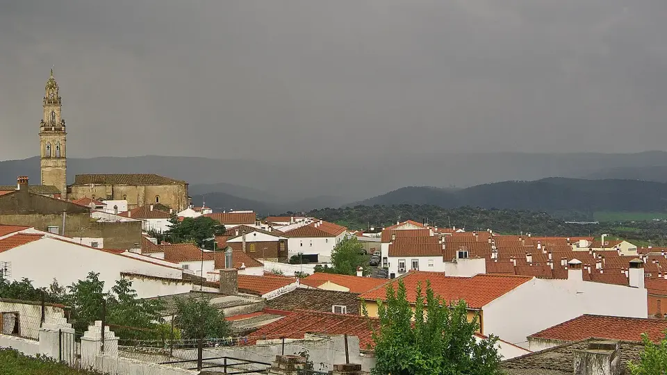 Tejados rojos de Jerez de los Caballeros con la torre de la iglesia de Santa Catalina y las sierras al fondo bajo nubes oscuras