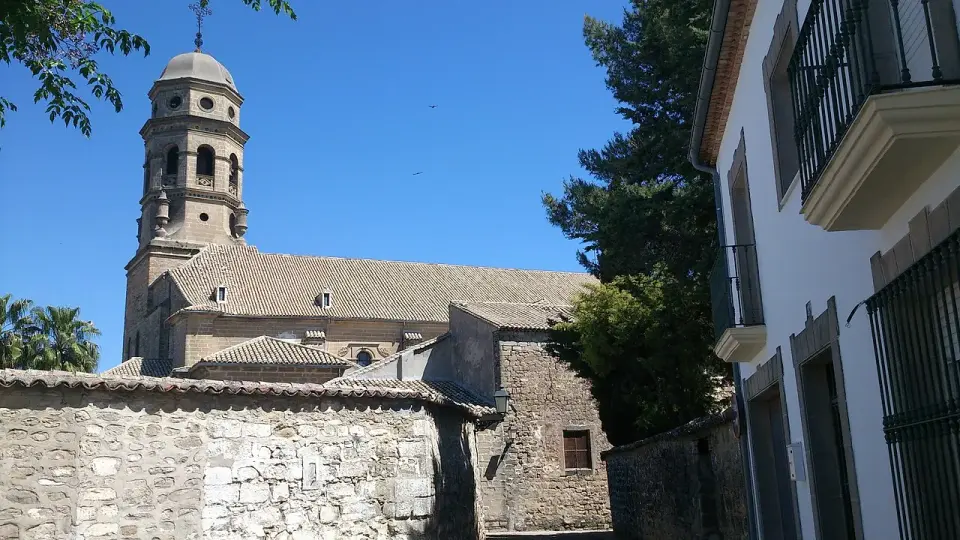 Torre y muros de piedra de la catedral de Baeza vistos desde una calle estrecha con fachadas blancas y rejas