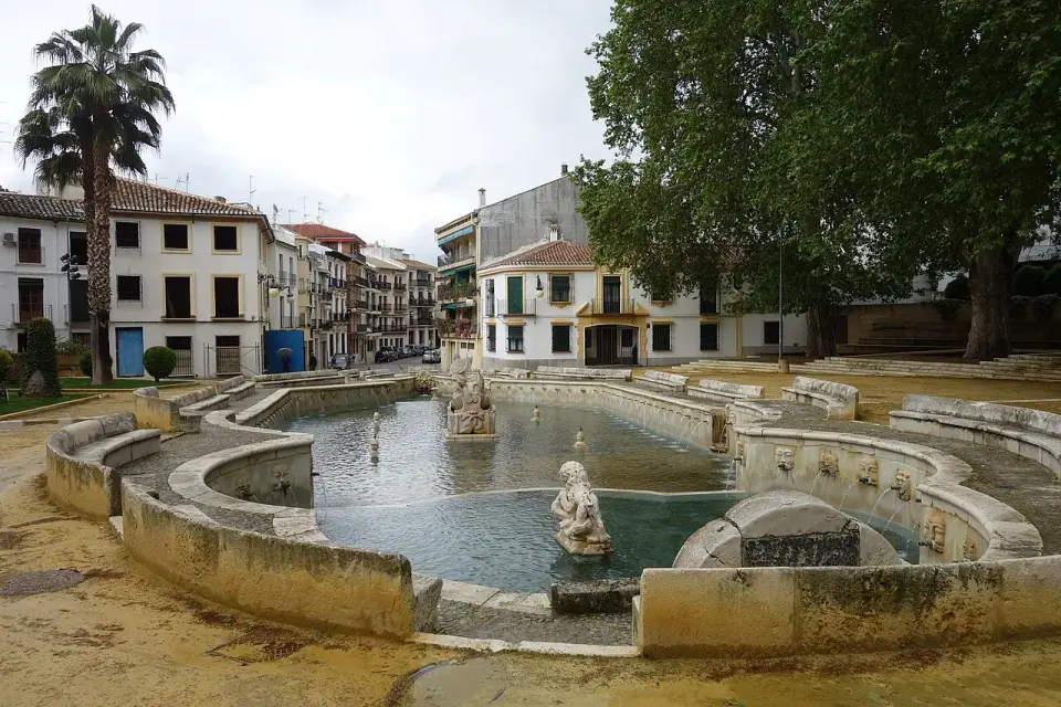 Estanque barroco de la Fuente del Rey en Priego de Córdoba, con esculturas y caños de agua, rodeado de casas blancas y árboles