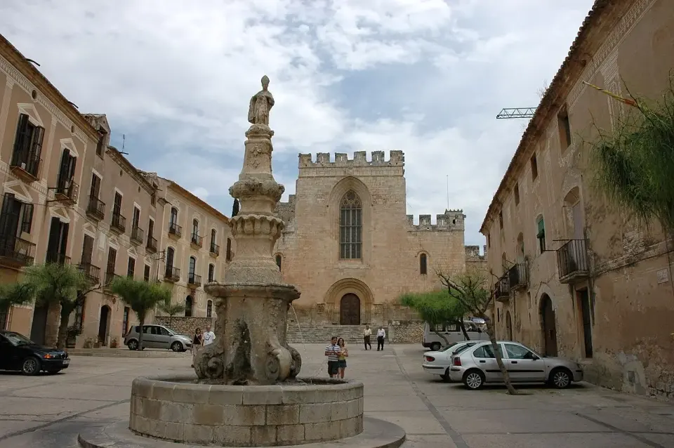 Plaza del monasterio de Santes Creus con una fuente coronada por una estatua y la fachada almenada de la iglesia al fondo