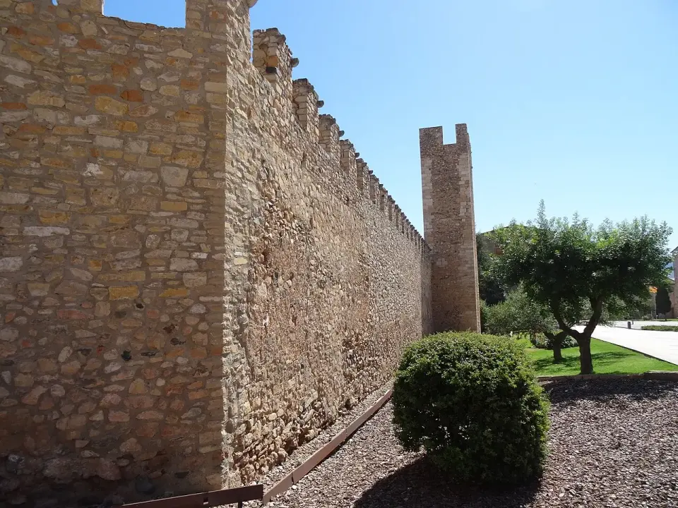 Lienzo de la muralla medieval de Montblanc con almenas y una torre, junto a un jardín