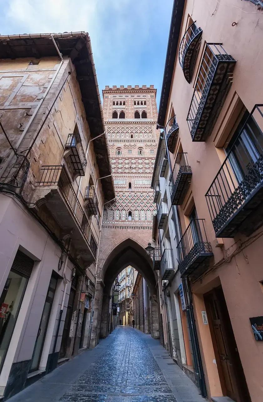 Torre mudéjar de El Salvador en Teruel, de ladrillo decorado con cerámica verde y blanca, sobre una calle estrecha con arco