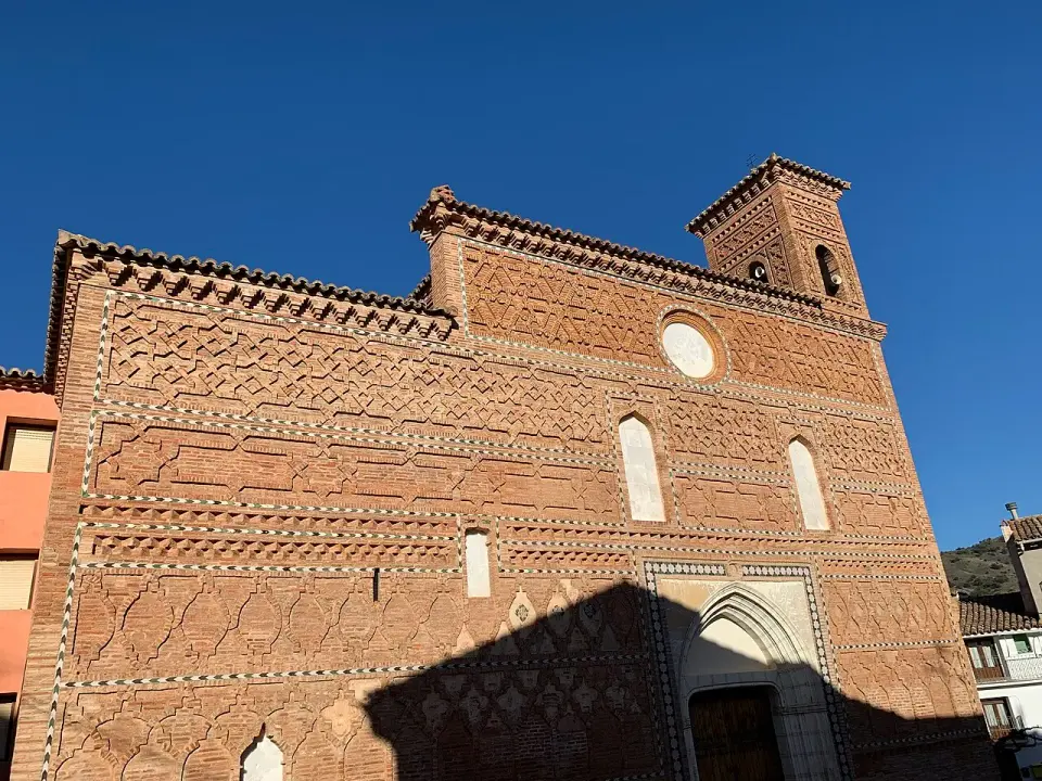 Fachada de ladrillo de la iglesia de Santa María de Tobed, con decoración mudéjar de rombos y un rosetón, bajo un cielo azul
