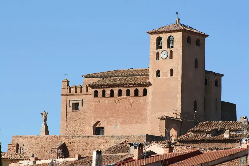 Iglesia de Santa Tecla en Cervera de la Cañada, de ladrillo rosado, con su torre campanario sobre los tejados del pueblo