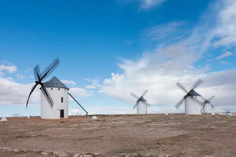 Molinos de viento blancos con tejado cónico negro en la Sierra de los Molinos de Campo de Criptana, bajo un cielo azul con nubes