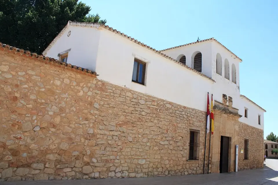 Casa encalada de El Toboso con zócalo y muro de mampostería, ventanas con reja y banderas en la fachada