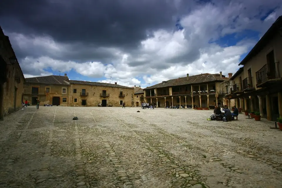 Plaza Mayor de Pedraza, amplia y empedrada, rodeada de casas con soportales bajo un cielo de nubes