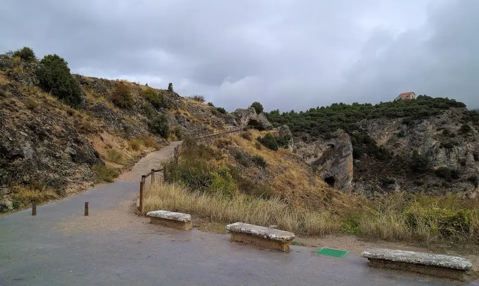 Camino con bancos de piedra junto a las rocas y la cueva del Ventano del Diablo, en la ladera sobre la hoz del Júcar