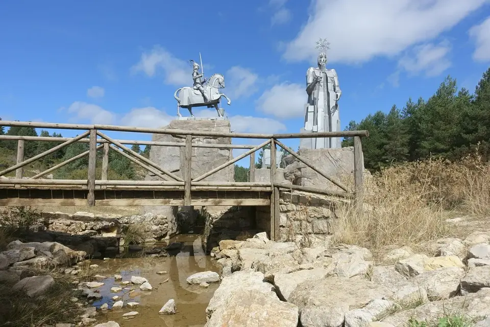 Monumento al nacimiento del río Tajo, con una figura a caballo y una estatua metálica sobre las rocas, junto a una pasarela de madera