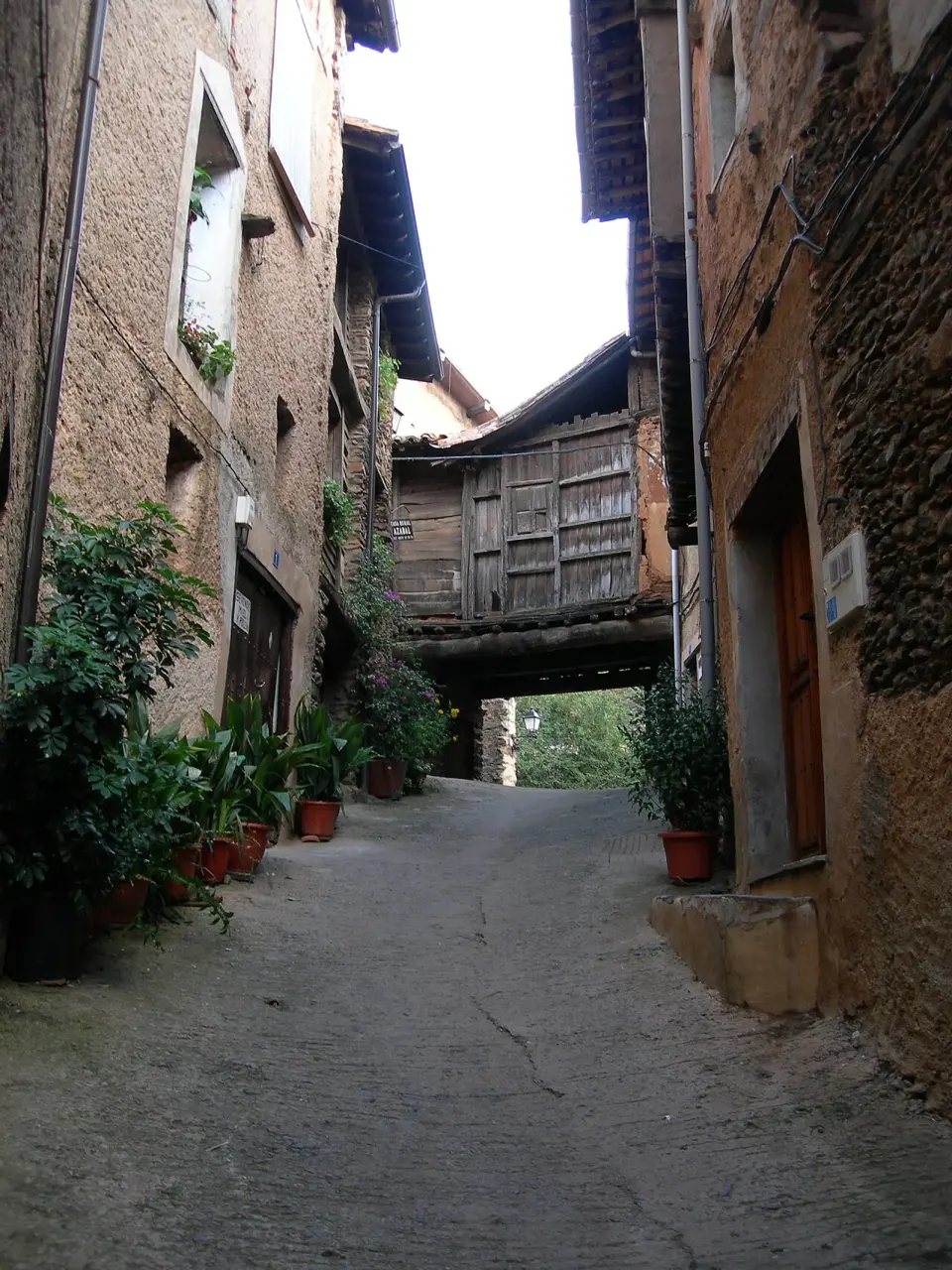 Calle empinada de Robledillo de Gata con casas de adobe y piedra y un pasadizo de madera al fondo