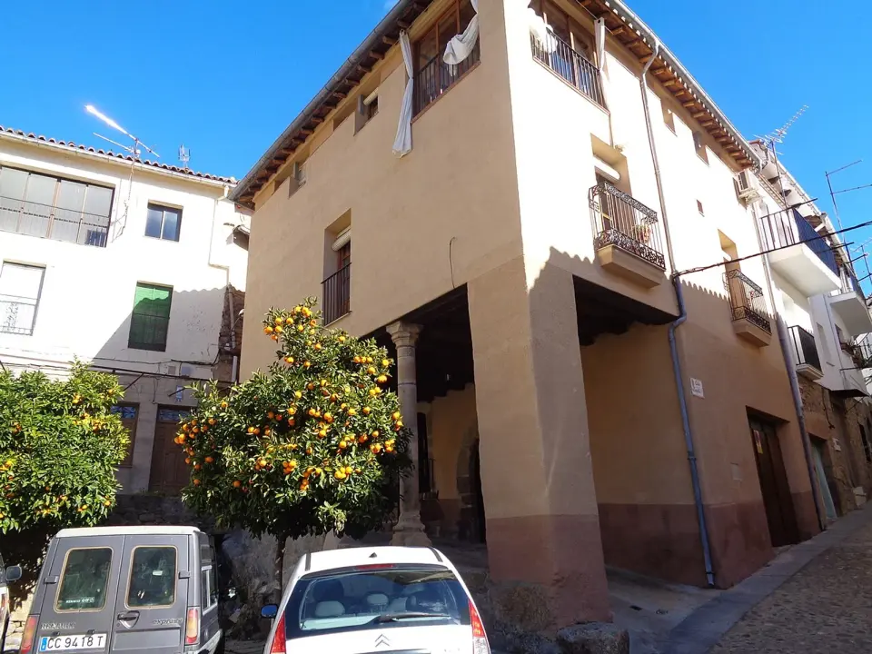 Casa de Gata con la planta baja sobre pilares de piedra, junto a dos naranjos cargados de fruta