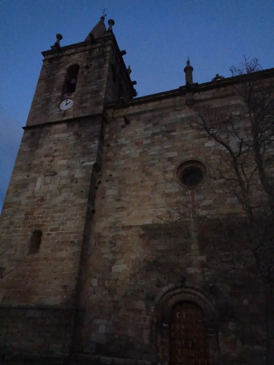 Torre y fachada de piedra de la iglesia de Nuestra Señora del Buen Varón de Hoyos al anochecer
