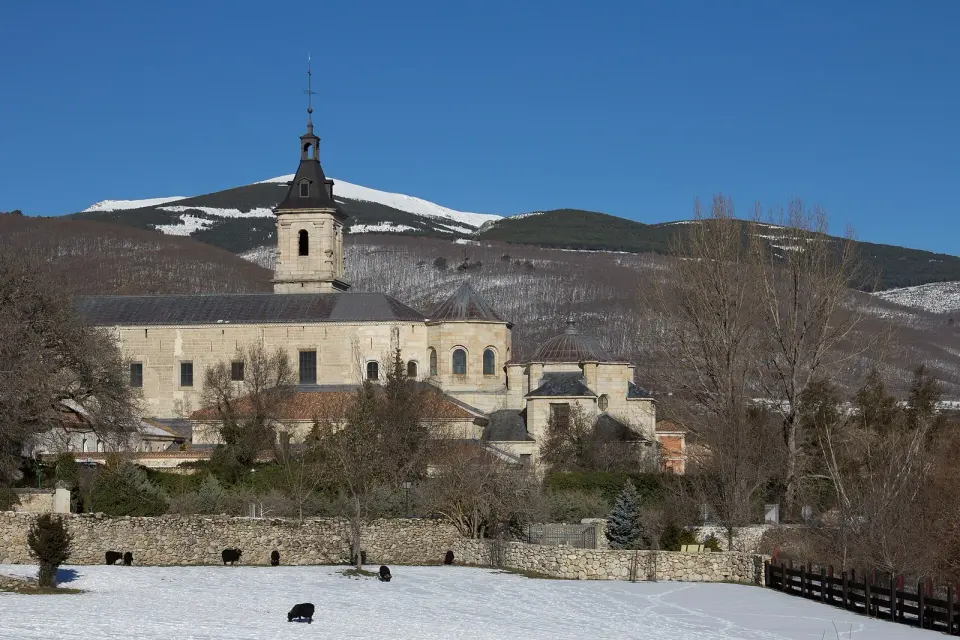 Monasterio de Santa María de El Paular, con su torre y sus cúpulas de piedra, rodeado de prados nevados y montañas al fondo