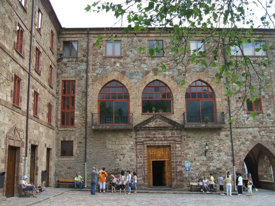 Fachada de piedra del monasterio de Valvanera con ventanales de arco rojos y visitantes en la explanada