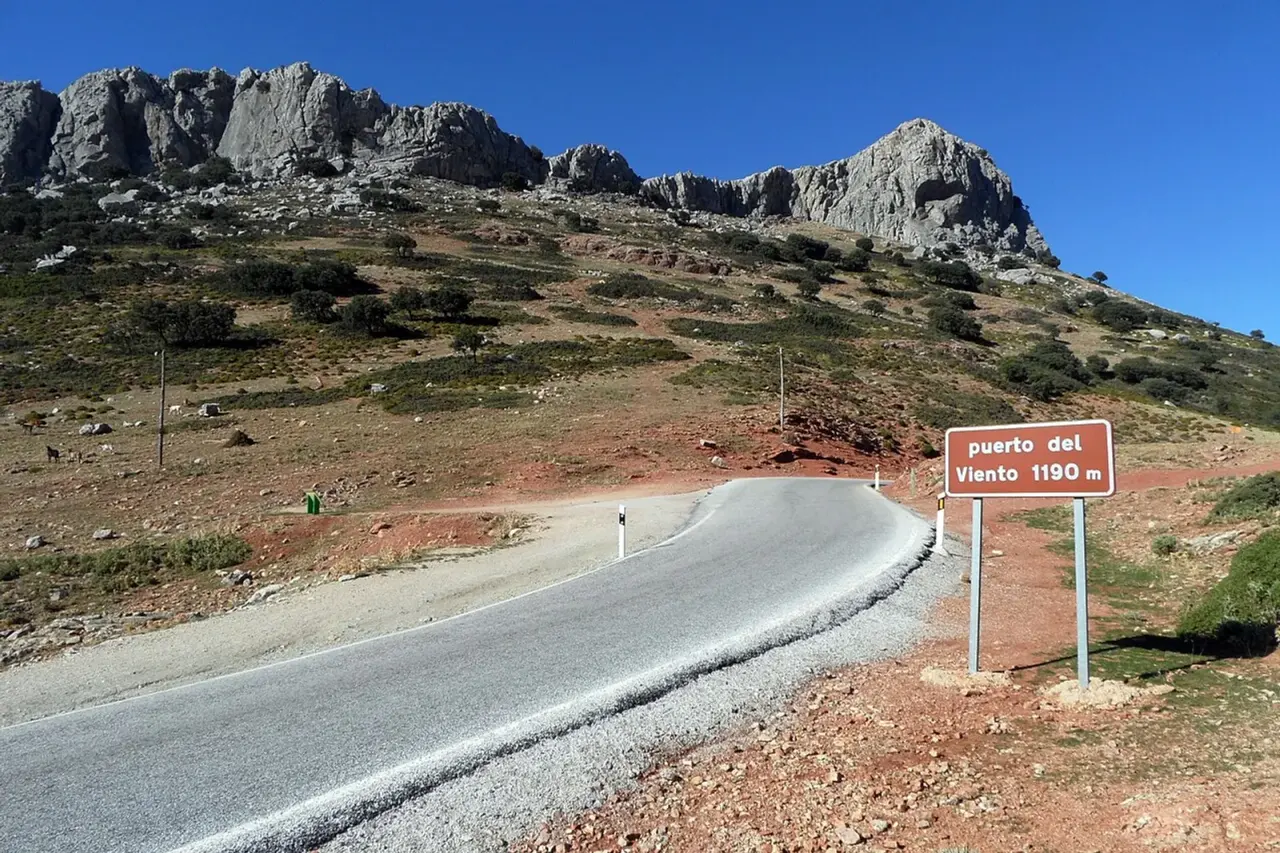 Carretera A-366 en el puerto del Viento, con el cartel marrón del puerto junto a la calzada y crestas de roca caliza bajo un cielo azul