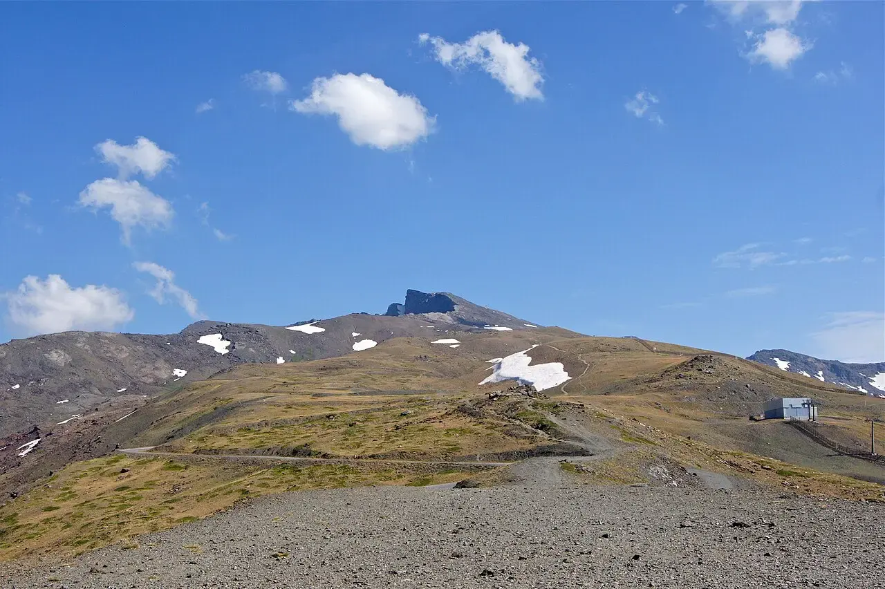 Pico Veleta con restos de nieve visto desde la antigua carretera de alta montaña de Sierra Nevada, entre lomas de pasto y piedra