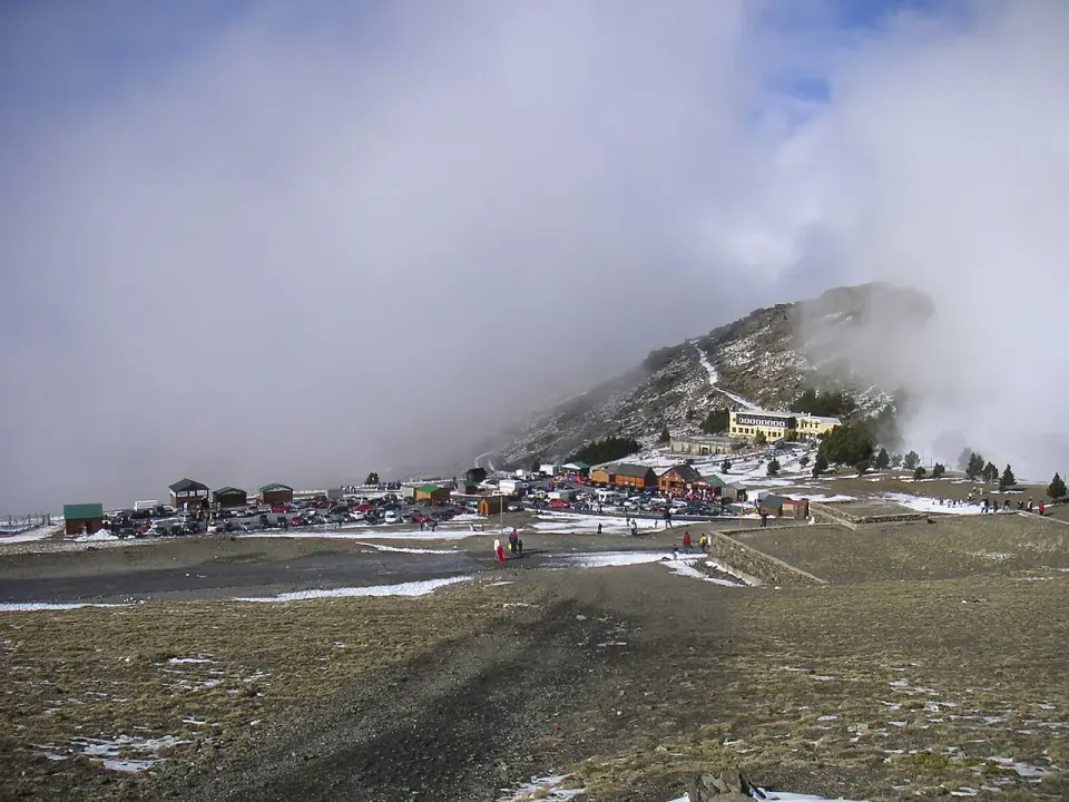 Aparcamiento y edificios de la Hoya de la Mora entre nubes, con restos de nieve en el suelo