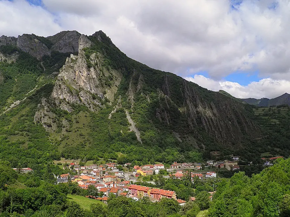 Pola de Somiedo con sus tejados rojos en el fondo del valle, bajo una montaña escarpada cubierta de vegetación