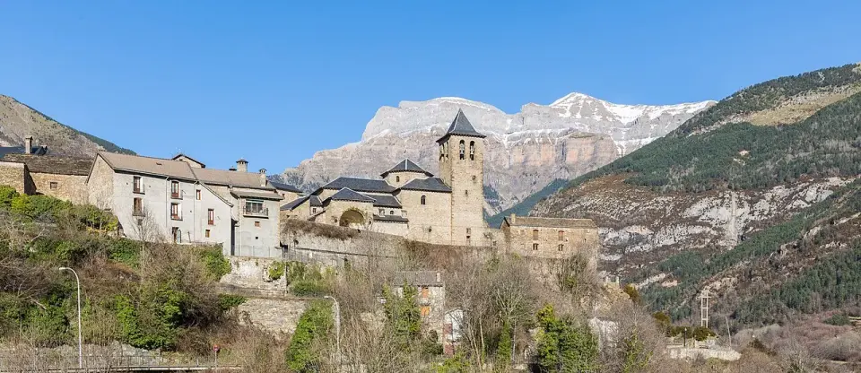 Pueblo de Torla con casas de piedra y su iglesia, frente a las paredes rocosas del valle de Ordesa con nieve en las cumbres