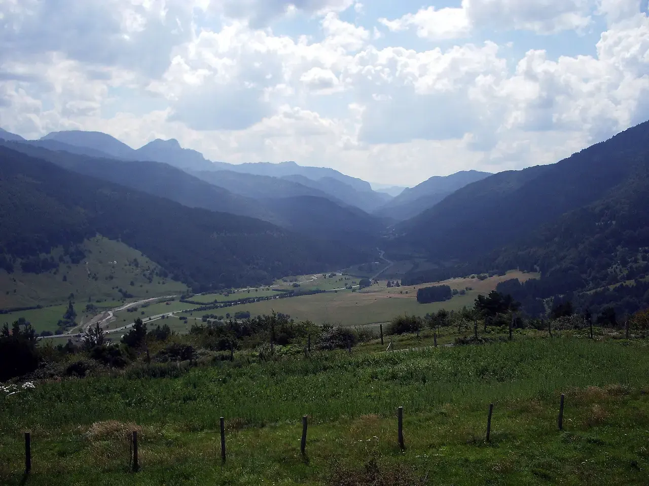 Valle de Belagua visto desde la Venta de Juan Pito, con praderas en el fondo, laderas de bosque y la carretera serpenteando