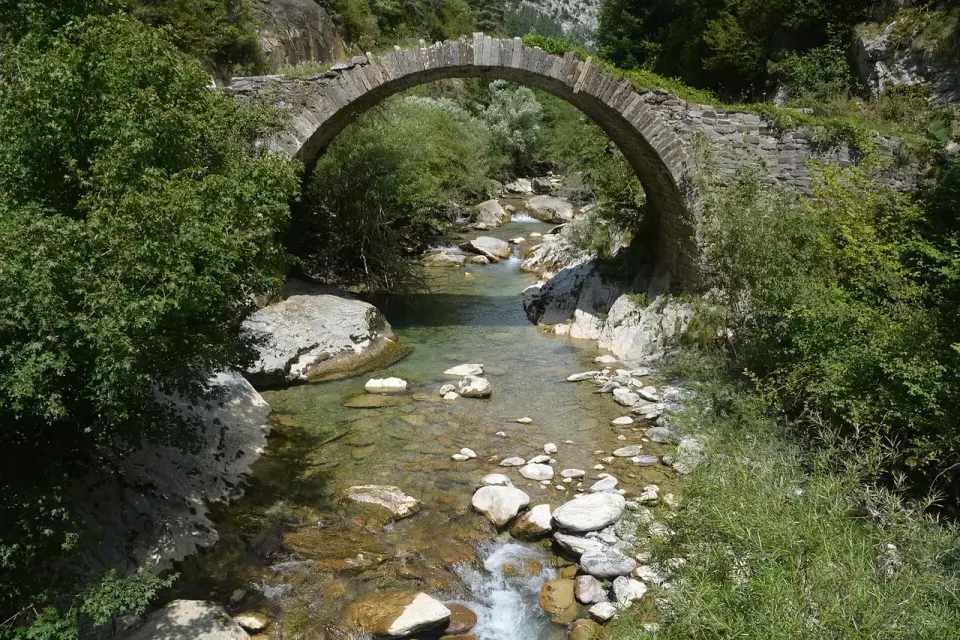 Puente de piedra de un solo arco sobre el río Belagua, con agua clara entre rocas y vegetación, en Isaba