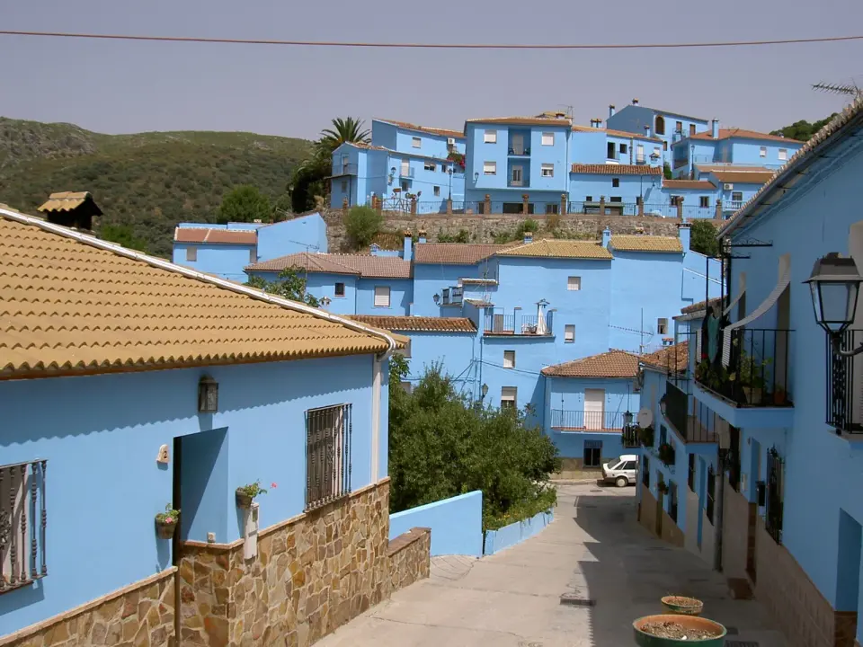 Calle en cuesta de Júzcar con todas las fachadas pintadas de azul y los tejados de teja árabe, y el monte al fondo