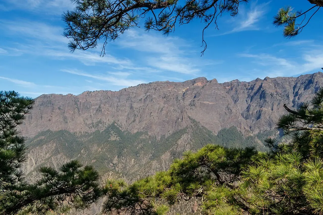 Paredes de la Caldera de Taburiente con crestas rocosas bajo un cielo azul, enmarcadas por ramas de pino canario